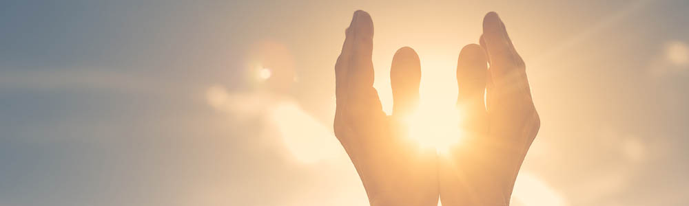 Close-up of hands up in prayer around the sun